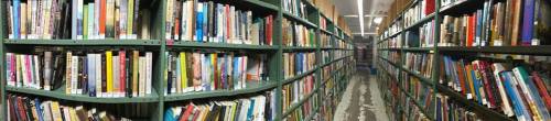 A panoramic view of a library aisle filled with books on shelves, creating a cozy and inviting atmosphere.