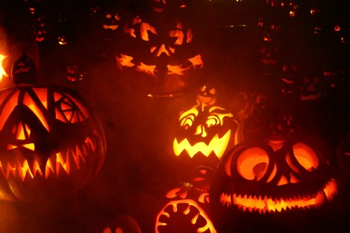 A spooky display of carved pumpkins glowing in the dark, surrounded by mist and eerie lighting.