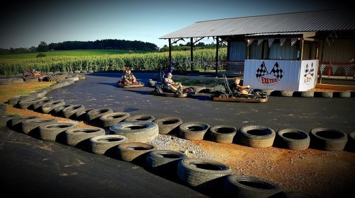 Go-karts racing on a track surrounded by tires, with a cornfield and a shelter in the background.