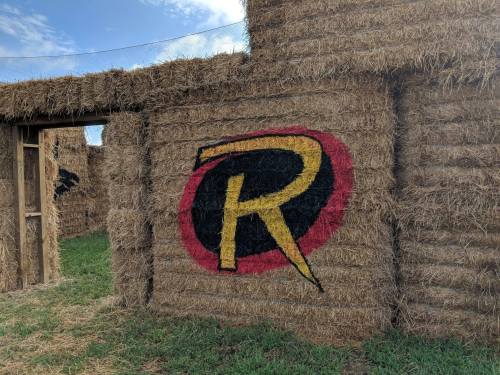 A hay bale structure featuring a large painted "R" in red and yellow against a black circle.
