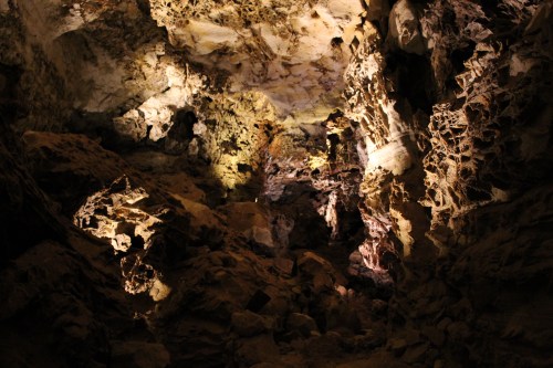 Dimly lit cave interior with rugged rock formations and shadows creating a mysterious atmosphere.