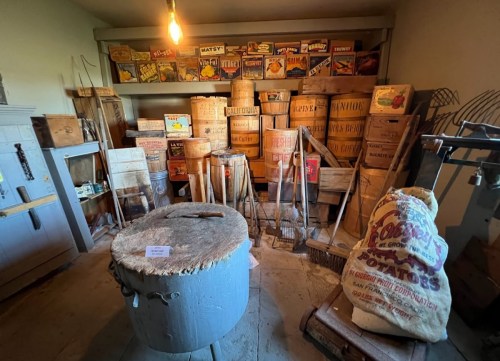A vintage storage room filled with wooden crates, barrels, and tools, showcasing old-fashioned items and signage.