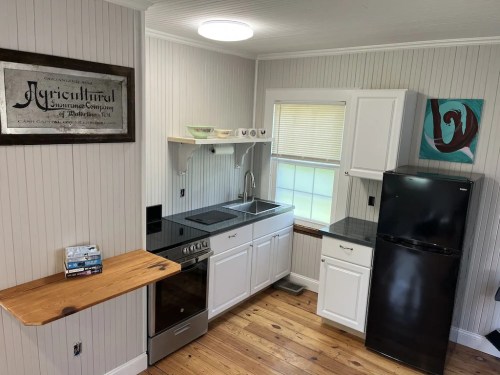 A modern kitchen with white cabinets, a black fridge, a wooden countertop, and a window letting in natural light.