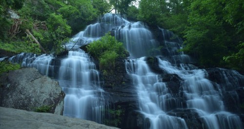 A serene waterfall cascading over rocks, surrounded by lush green trees and foliage.