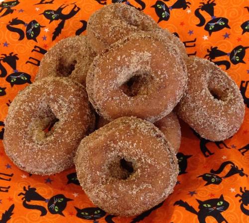 A pile of cinnamon sugar donuts on an orange plate decorated with black cats and Halloween motifs.