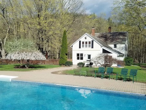 A serene backyard scene featuring a pool, a house, and lush greenery with trees in the background.