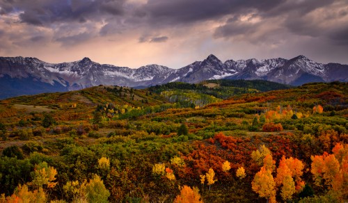 A scenic view of mountains with snow-capped peaks, surrounded by vibrant autumn foliage in shades of orange and yellow.