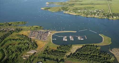 Aerial view of a marina surrounded by green fields and water, with boats docked and a parking area nearby.