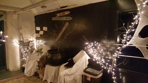 A dimly lit room with decorated branches, fairy lights, and a large pot, creating a cozy, festive atmosphere.