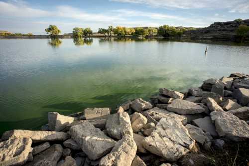 A serene lake surrounded by rocky shores and trees, reflecting a clear sky and gentle ripples on the water's surface.