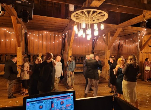 A lively gathering in a rustic barn with people dancing and socializing under warm string lights.
