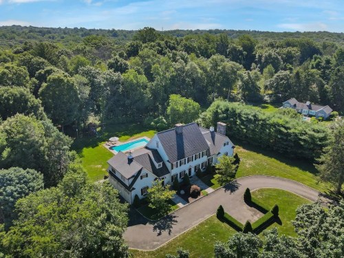 Aerial view of a large white house with a pool, surrounded by lush greenery and trees.