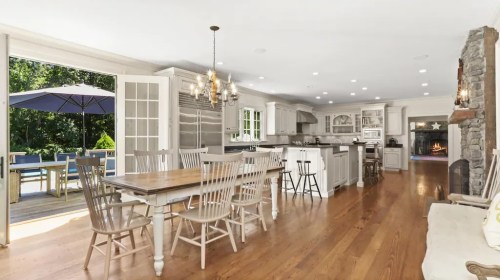 Bright, modern kitchen with a dining table, white cabinetry, and large windows overlooking a patio and pool area.