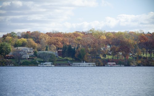 A serene lake view with colorful autumn trees lining the shore and houses nestled among the foliage.