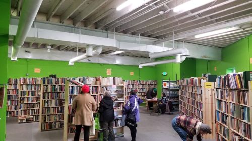 A vibrant green room filled with bookshelves and people browsing books in a cozy library setting.