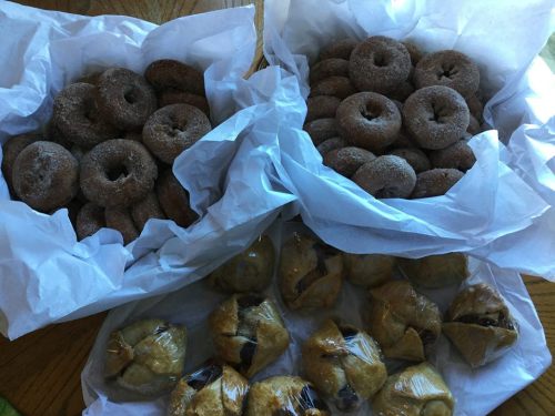 Three baskets of freshly baked donuts and pastries, wrapped in white paper, arranged on a wooden table.