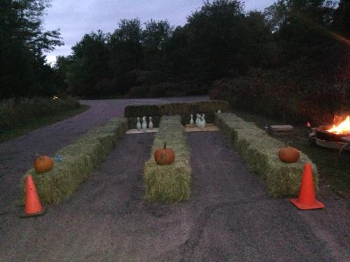 A bowling setup with hay bales, pumpkins, and traffic cones, set in a dimly lit outdoor area.