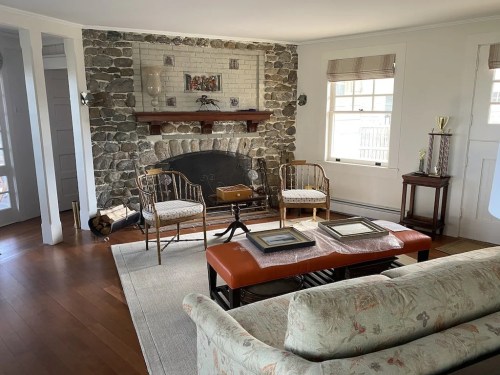 Cozy living room with a stone fireplace, wooden furniture, and a light-colored sofa on a hardwood floor.
