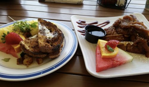 A plate of French toast with fruit and potatoes, alongside a plate of pancakes with syrup and fruit slices.