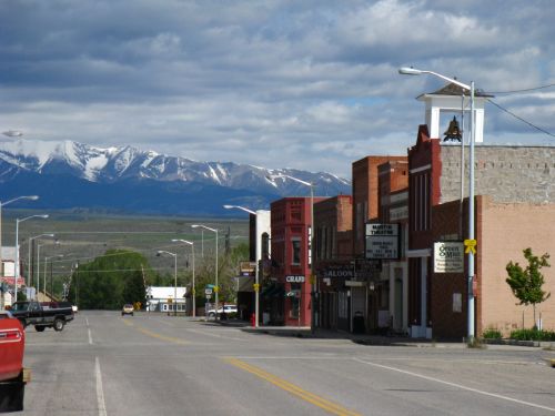 A quiet street in a small town with historic buildings and snow-capped mountains in the background under a cloudy sky.