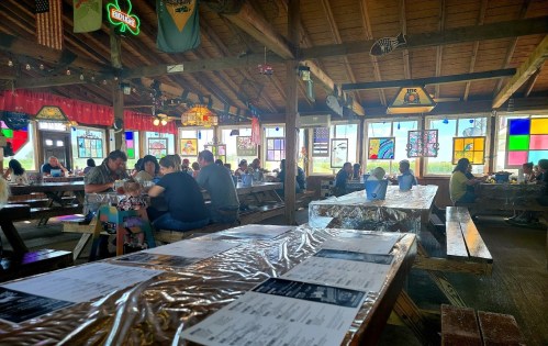 A lively restaurant interior with wooden tables, colorful stained glass windows, and diners enjoying their meals.