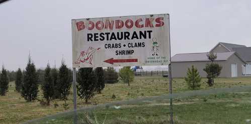 Sign for Boondocks Restaurant featuring crabs, clams, and shrimp, with a greenhead fly logo in a rural setting.