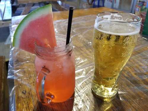 A refreshing pink drink with a watermelon slice and a glass of golden beer on a wooden table.