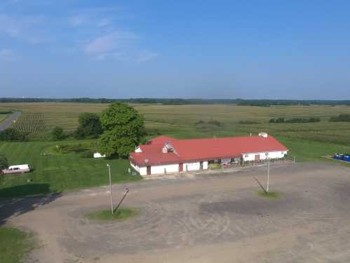 Aerial view of a rural building with a red roof, surrounded by green fields and a clear blue sky.