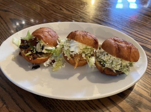 Three small sandwiches on a plate, filled with lettuce, cheese, and various toppings, on a wooden table.