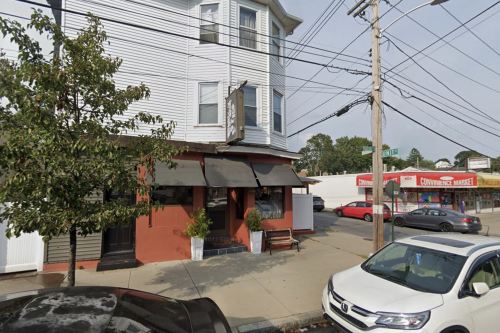 A street view of a multi-story building with a restaurant entrance, surrounded by power lines and parked cars.