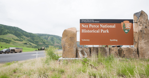 Sign for Nez Perce National Historical Park, with green hills and a highway in the background.