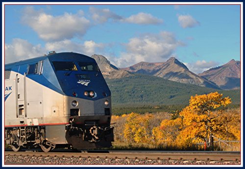 A train travels along tracks with colorful autumn trees and mountains in the background under a blue sky.