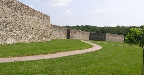 A winding path leads through a grassy area beside a stone wall under a clear blue sky.