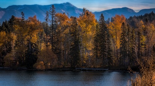 A serene lake surrounded by vibrant autumn trees and distant mountains under a clear sky.