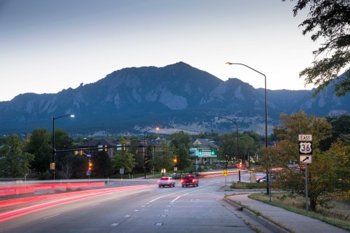 A scenic view of mountains at dusk, with light trails from cars on a road and traffic signals visible.