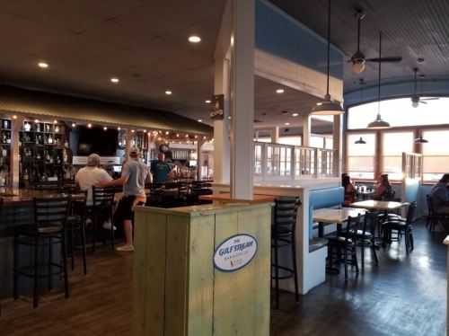 Interior of a casual restaurant with a bar, seating areas, and large windows, creating a bright and inviting atmosphere.