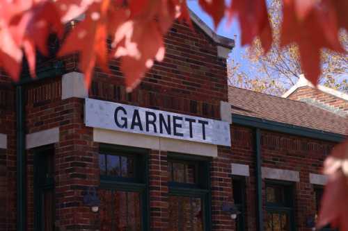 A brick building with a sign reading "GARNETT," framed by vibrant red autumn leaves.