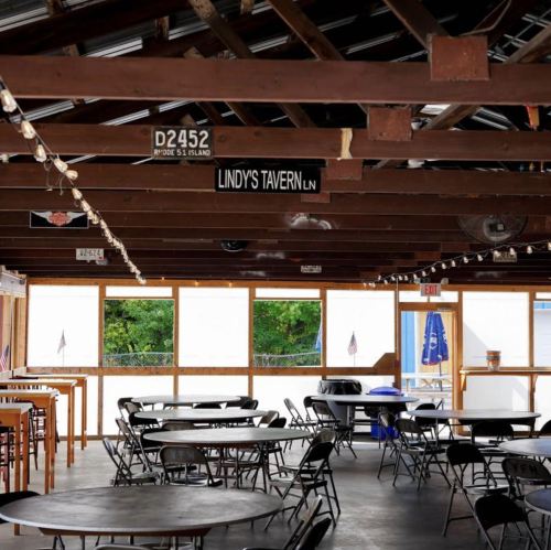 Interior of a tavern with wooden beams, tables, and large windows, featuring a sign for "Lindy's Tavern Lane."