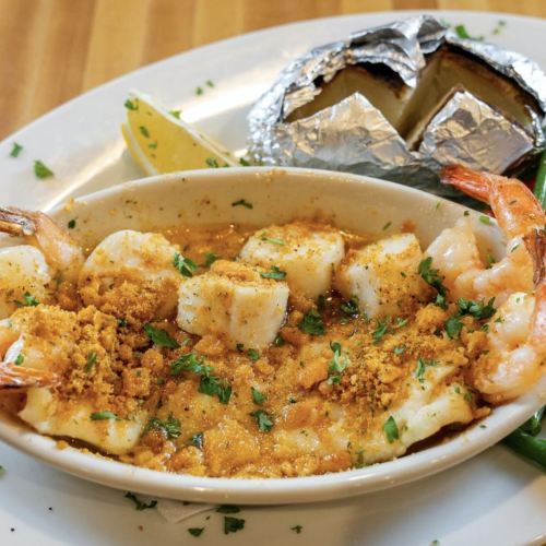 A dish featuring shrimp, fish, and breadcrumbs, served with a baked potato and lemon wedge on a white plate.