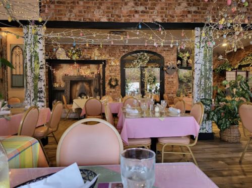 Cozy restaurant interior with pink tables, brick walls, and decorative lights, creating a warm, inviting atmosphere.