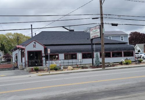 A gray and white restaurant with a sign, surrounded by landscaping and power lines, on a cloudy day.