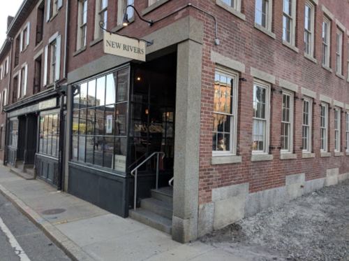 Exterior view of the New Rivers restaurant, featuring a brick building with large windows and a staircase entrance.