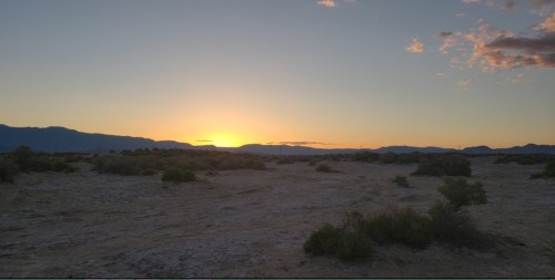 A serene desert landscape at sunset, with mountains in the background and soft clouds in the sky.