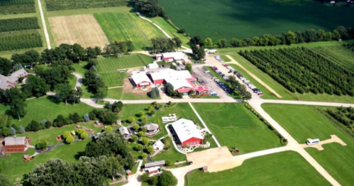 Aerial view of a farm with red buildings, green fields, and orchards, surrounded by well-maintained landscapes.