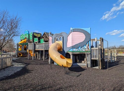 Colorful playground with a large slide, climbing structures, and a blue sky in the background.