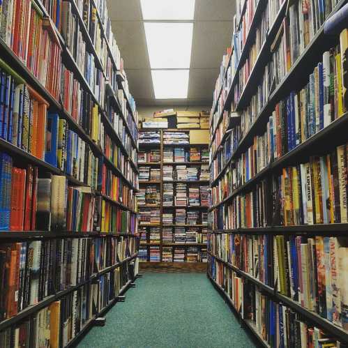A narrow aisle between tall bookshelves filled with colorful books in a well-lit library.
