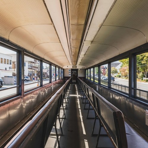 Interior of a train car with empty rows of seats and large windows, showcasing a bright, open space.