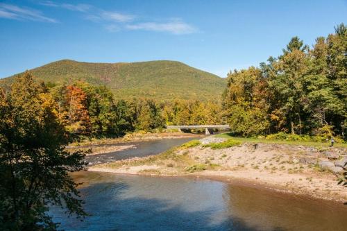 A serene river flows through a landscape of trees and a distant mountain under a clear blue sky.