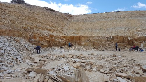 A stone quarry with workers extracting stone from the rocky terrain under a blue sky with scattered clouds.