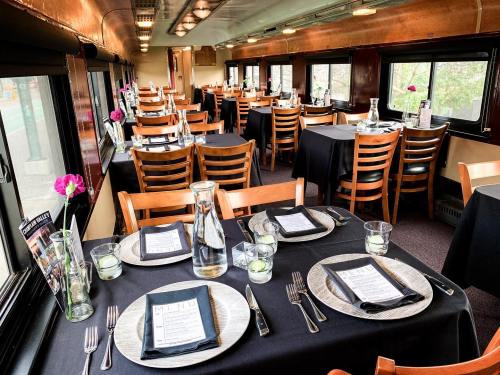 Elegant dining setup in a train car, featuring black tablecloths, plates, and flowers, with large windows and a cozy atmosphere.